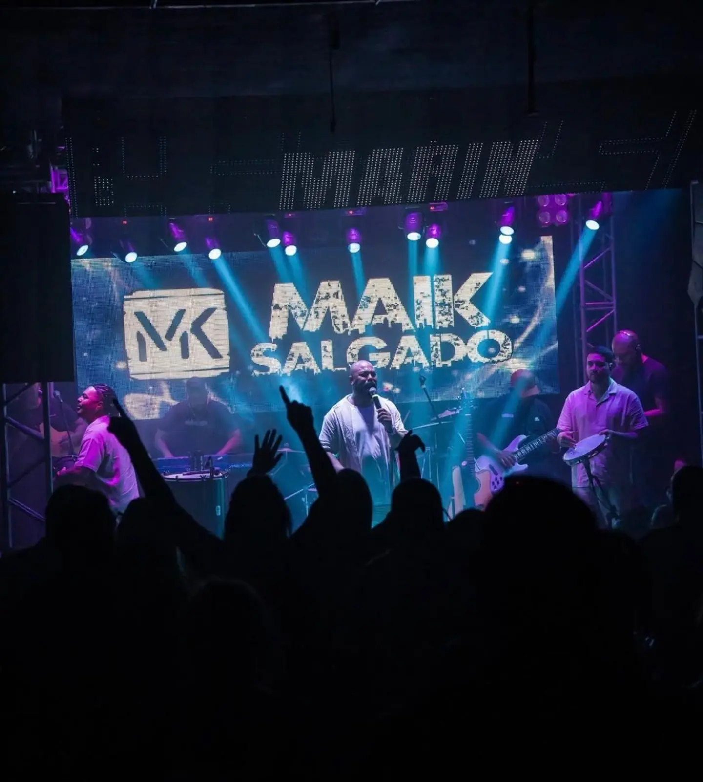 Maik Salgado & Banda se apresentando com banda completa, telão ao fundo
